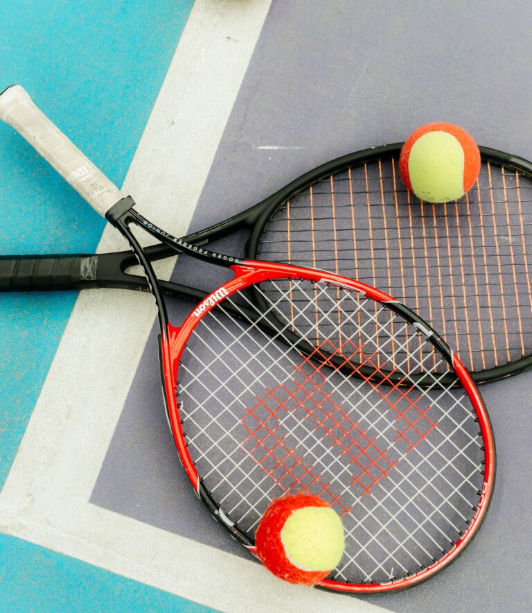 Two tennis rackets and balls on a vibrant blue court corner, ready for a match.